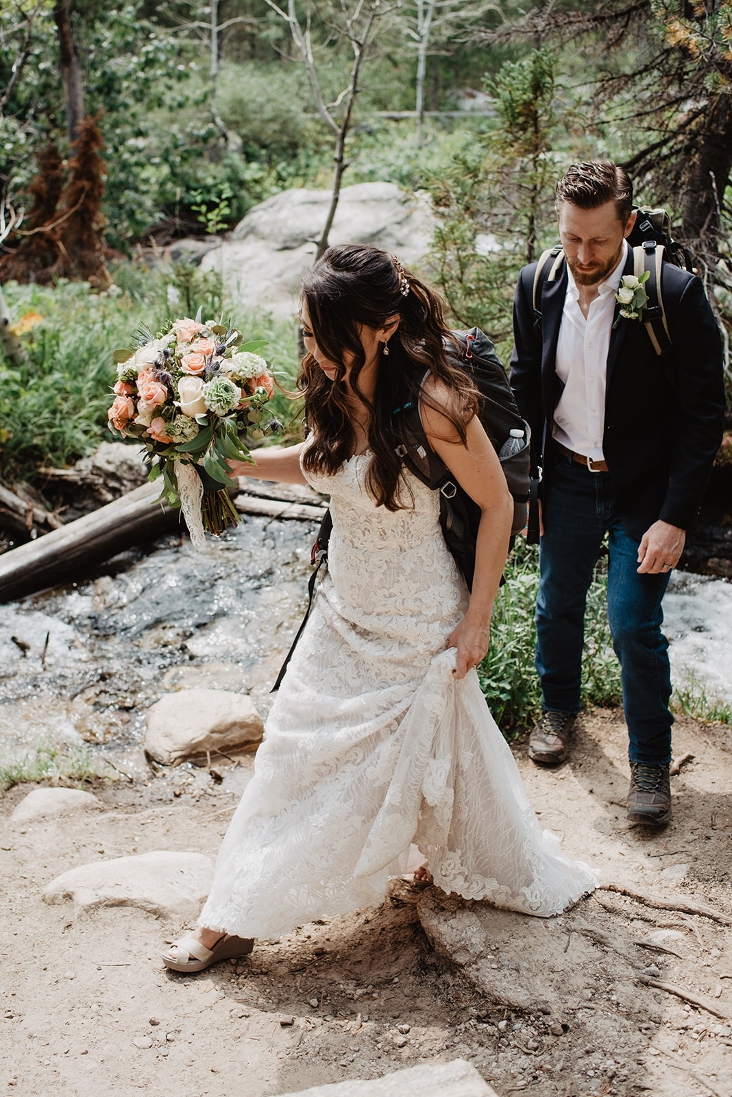 candid shot of bride and groom walking together on a hiking trail in their wedding gear and their backpacks on for their Taggart Lake weddings day