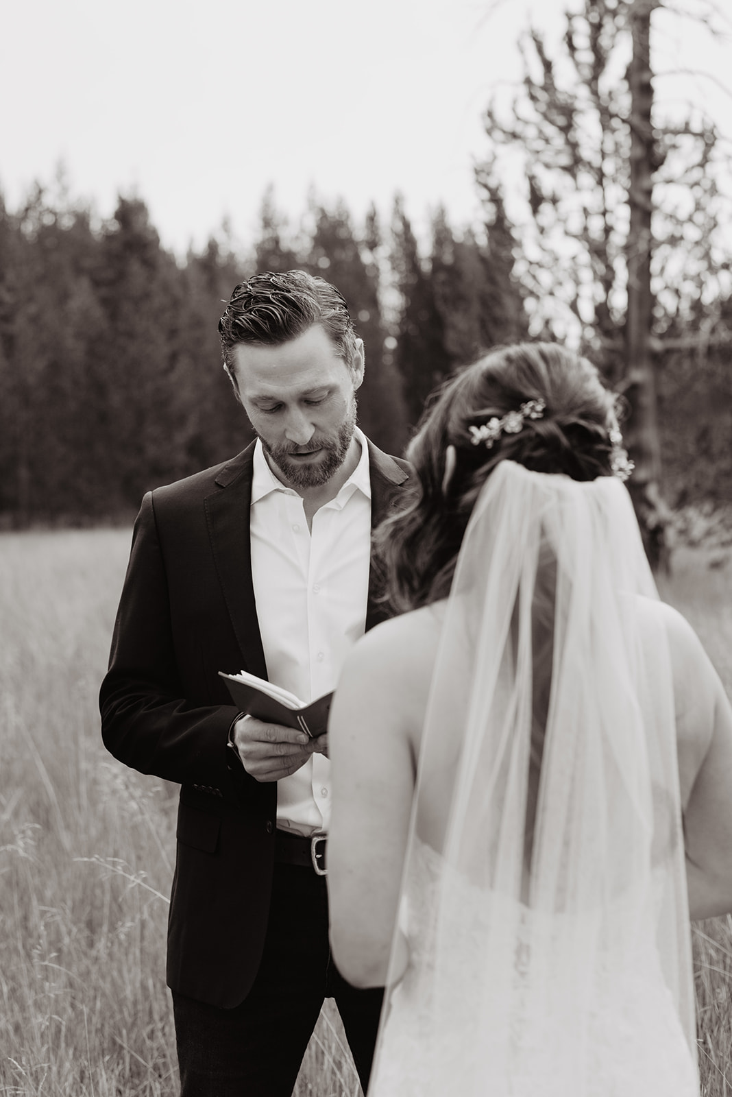 black and white picture of groom reading his vows to his bride in the Grand Tetons near Taggart Lake while the bride stands in front of him