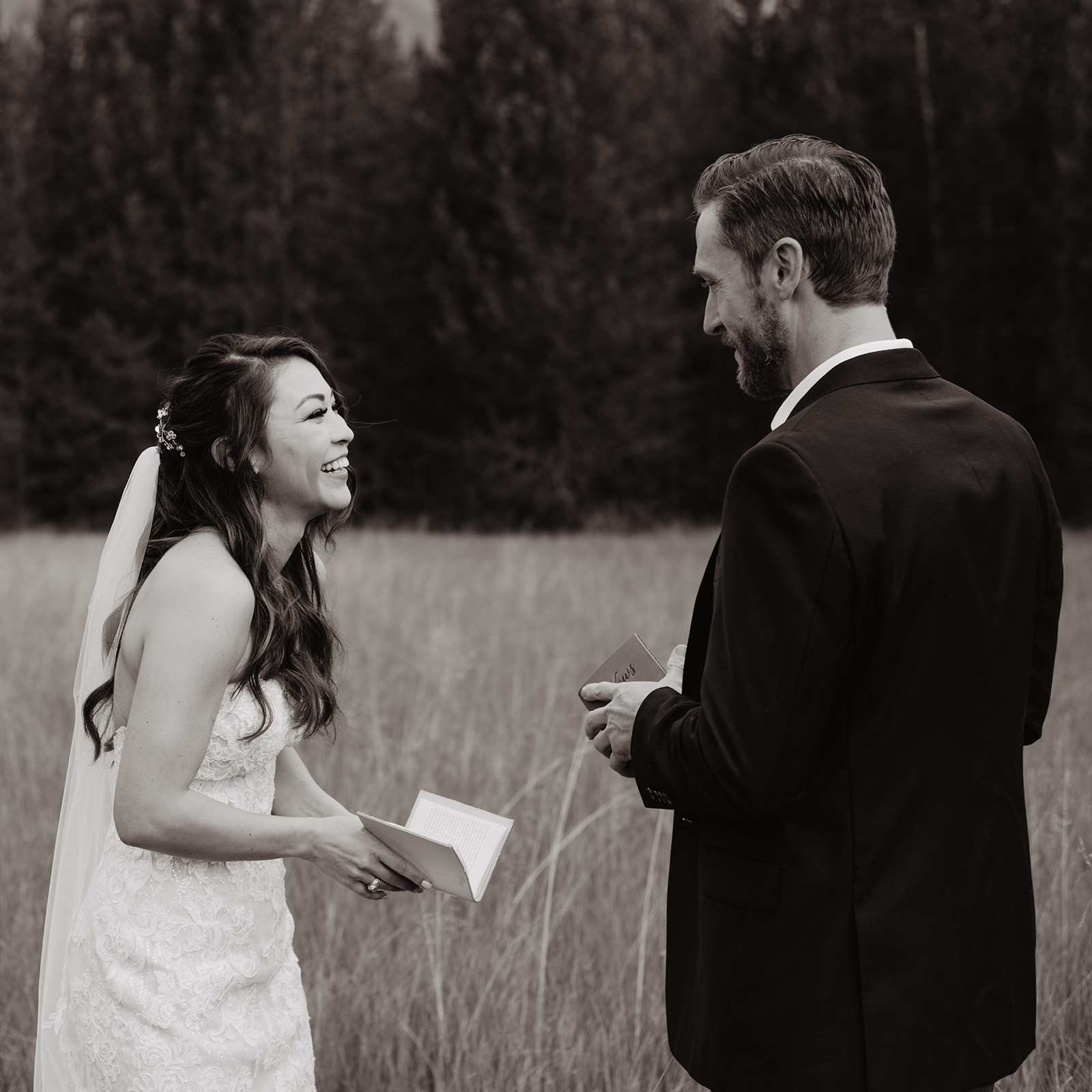 bride laughing during her private vow reading with her groom in the Grand Tetons on her Taggart Lake wedding day as her groom reads his vows