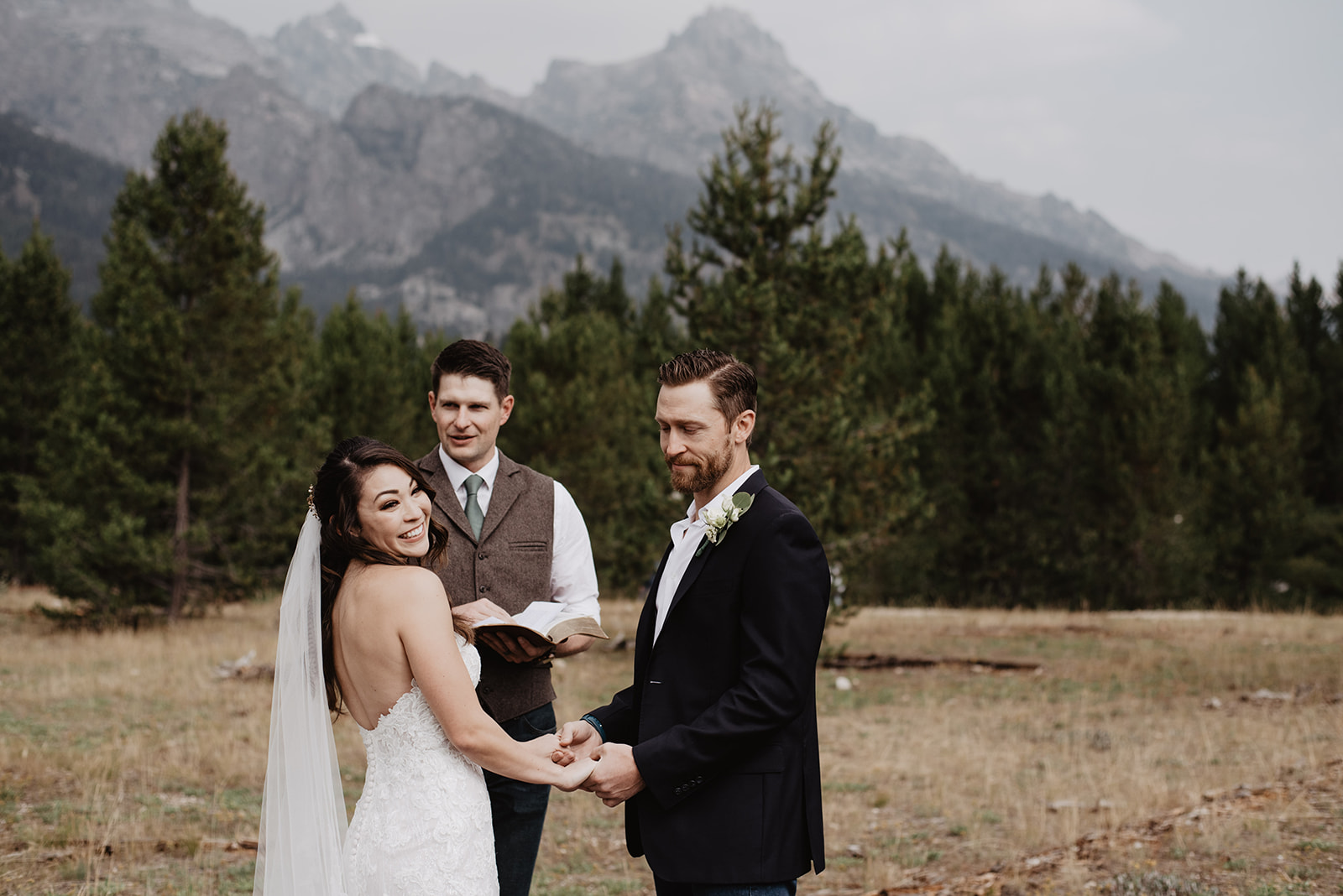 Taggart Lake wedding ceremony with bride smiling over her shoulder as she holds her grooms hands and the officiant marries the couple