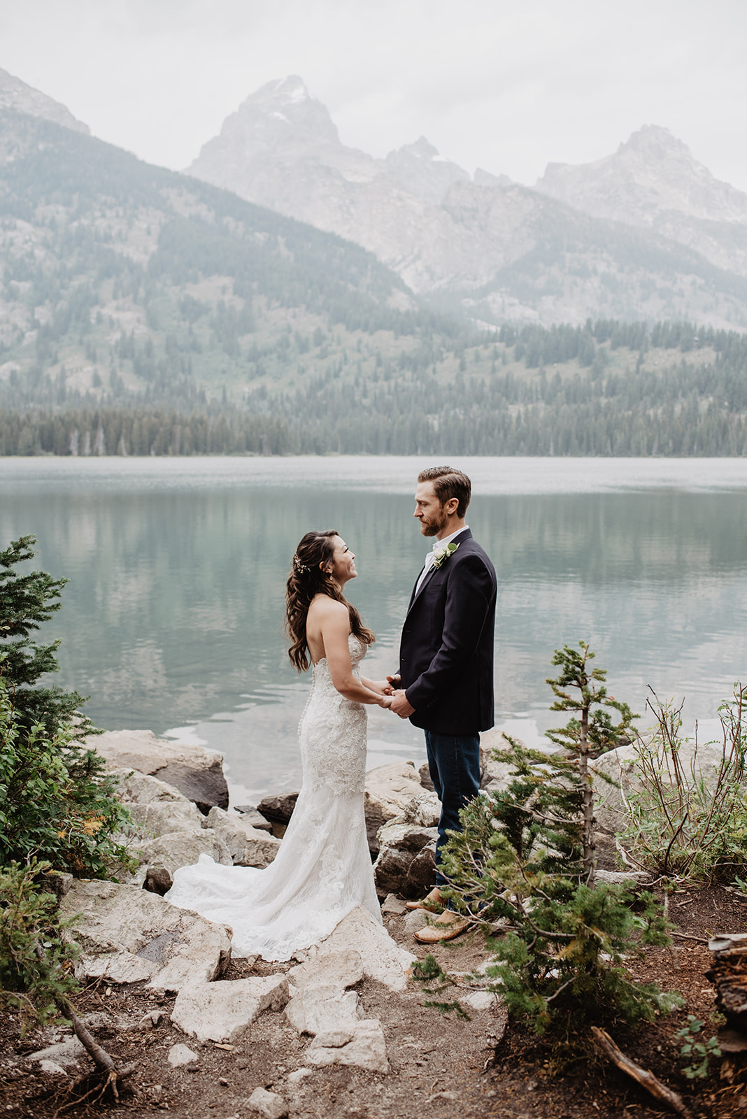 Taggart Lake Wedding with bride and groom holding hands together and looking at one another with Taggart Lake behind them and the Grand Tetons for their Grand Teton adventure wedding