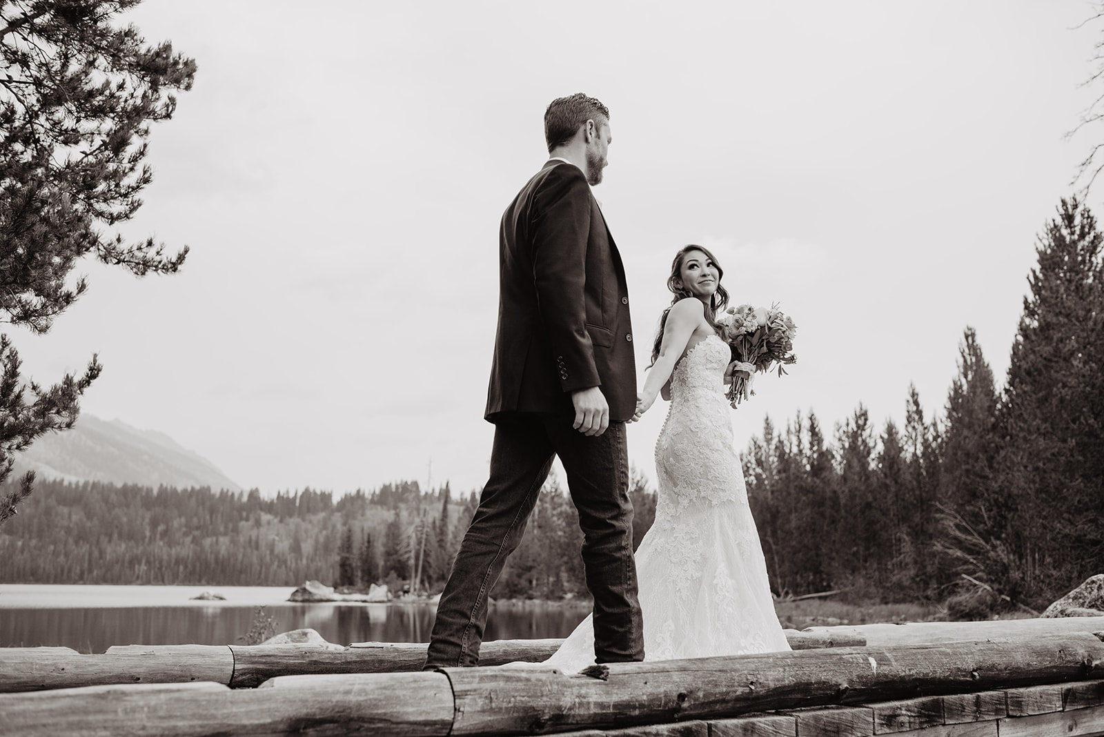 bride holding her grooms hand and walking a head of him as she leads him over a bridge