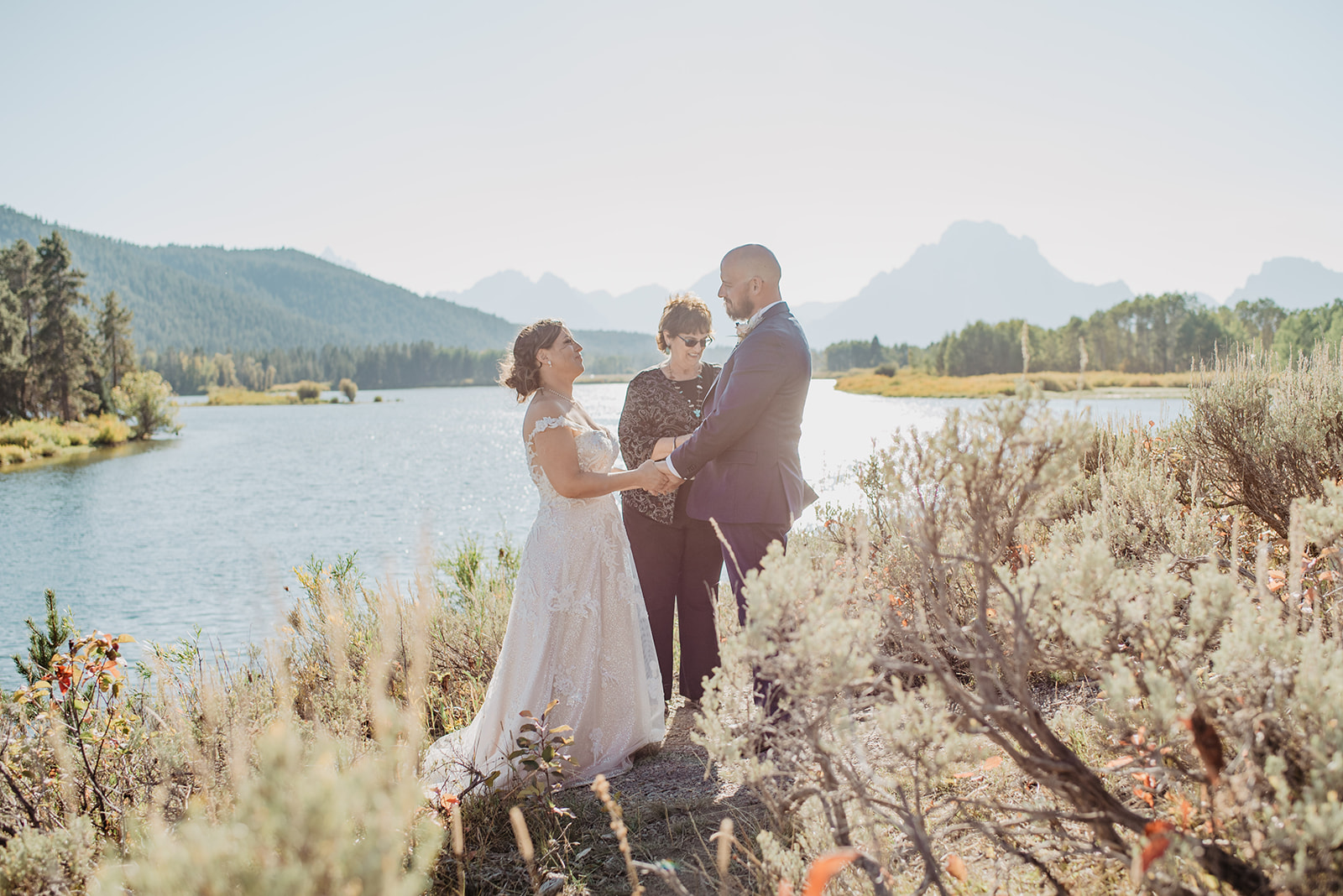 Onbow Bend Elopement ceremony next to Snake River in the Jackson Hole with the Tetons in the background as the bride and groom hold hands and are married by their wedding officiant