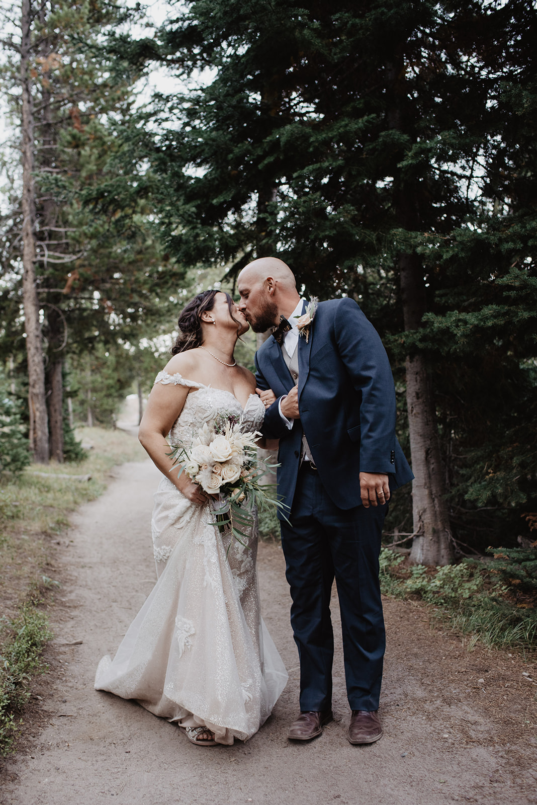 bride and groom kissing as they walk through the forest in the Grand Tetons on their wedding day while kissing and holding hands 