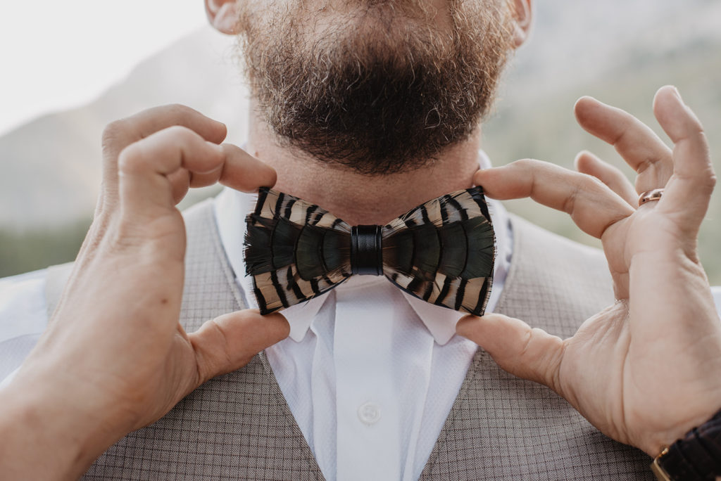 groom holding his feather bowtie for a detail shot for his Jackson Hole wedding photos
