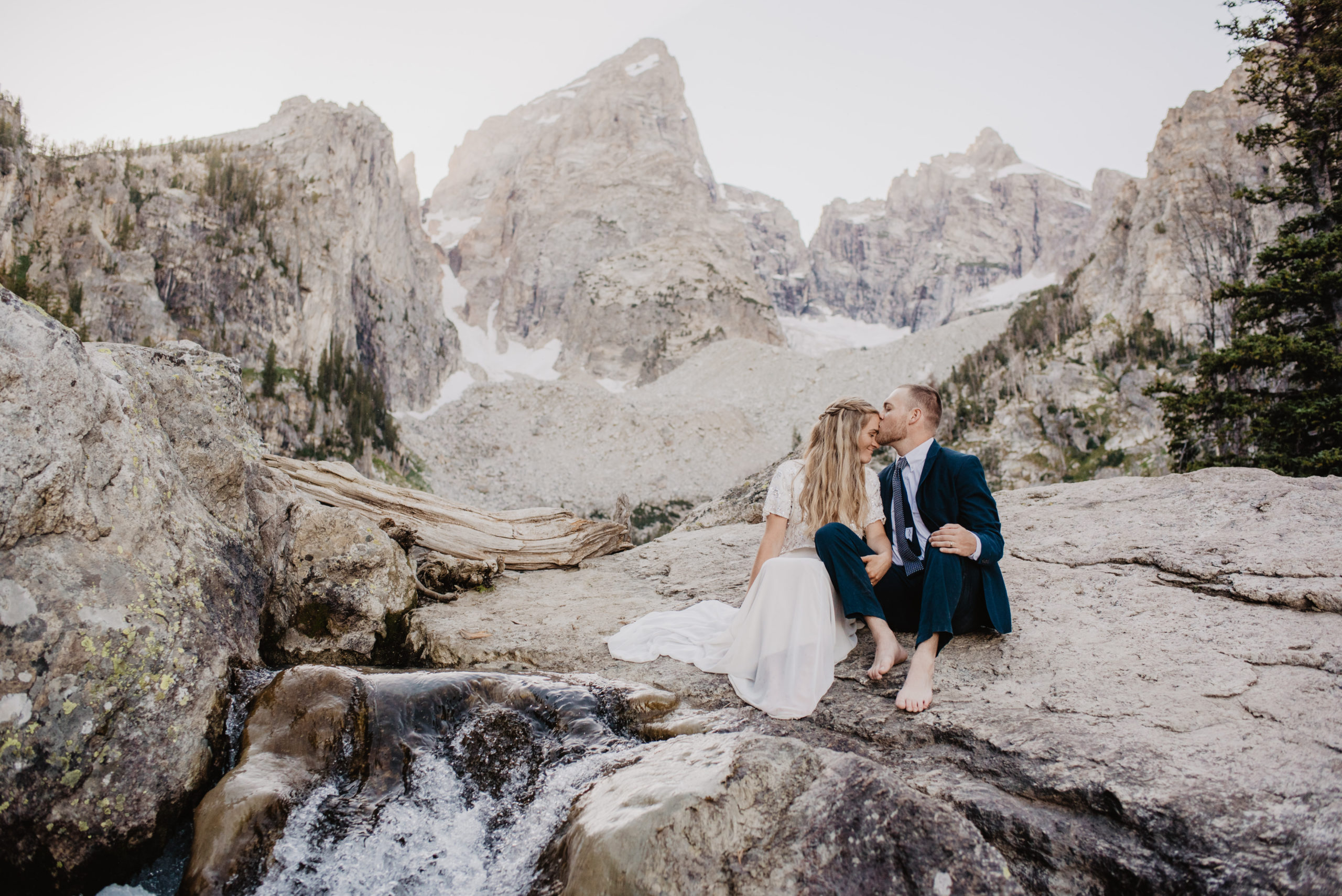 bride and groom sitting on a rock at Delta Lake for their National Park elopement with the groom kissing the brides forehead very romantically
