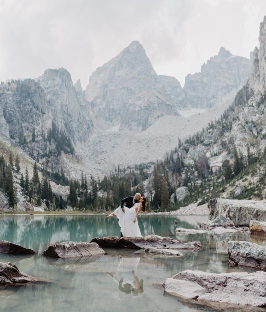 groom dips his bride in the middle of a lake in the Tetons