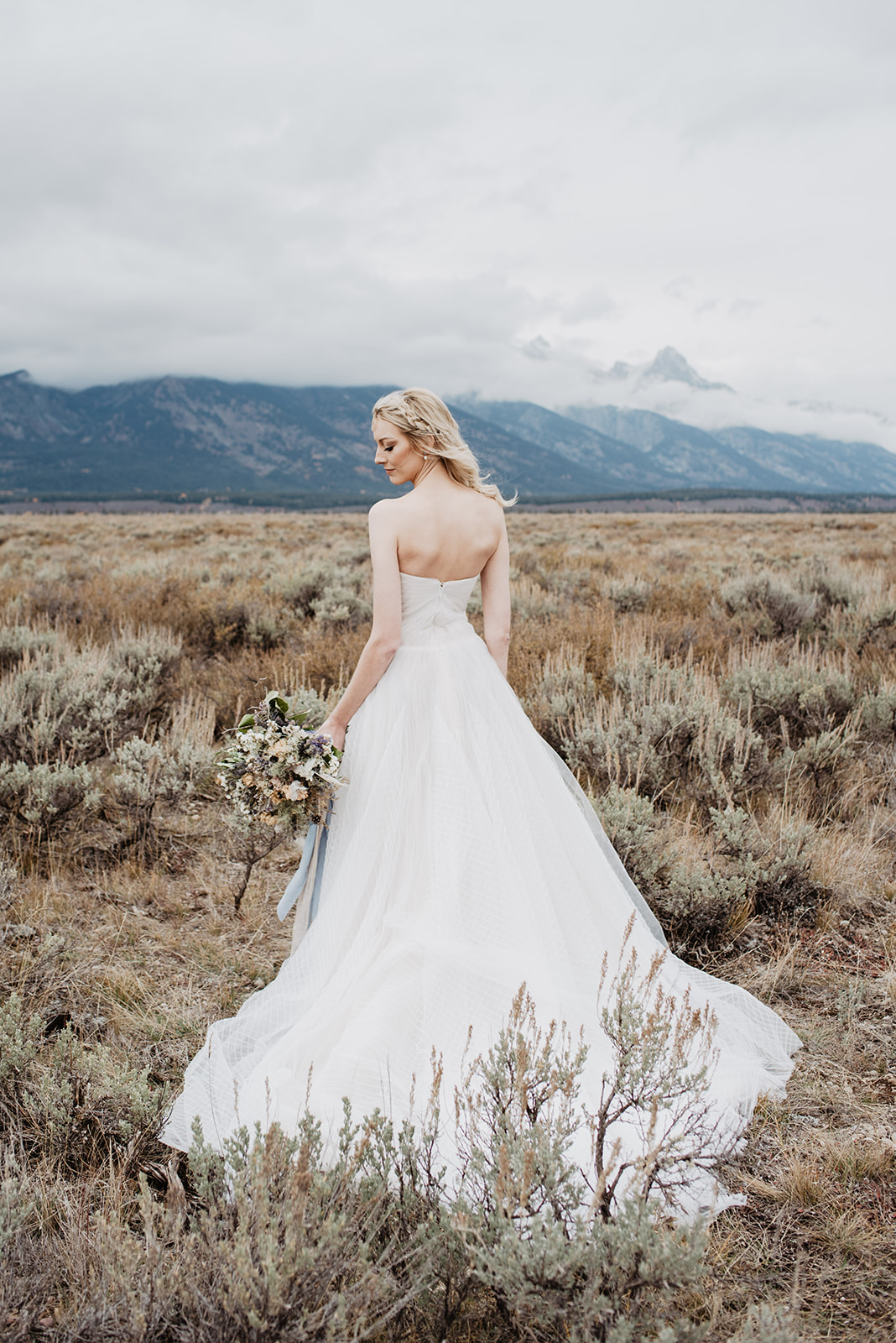 blonde bride standing with her back to the camera and looking over her shoulder with her eyes closed to show off the back of her white classic wedding dress