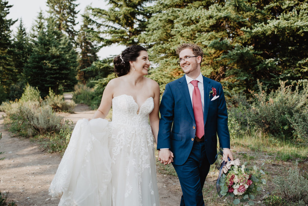 bride and groom hold hands and walk through the woods in the tetons for bridal pictures with jackson hole photographer