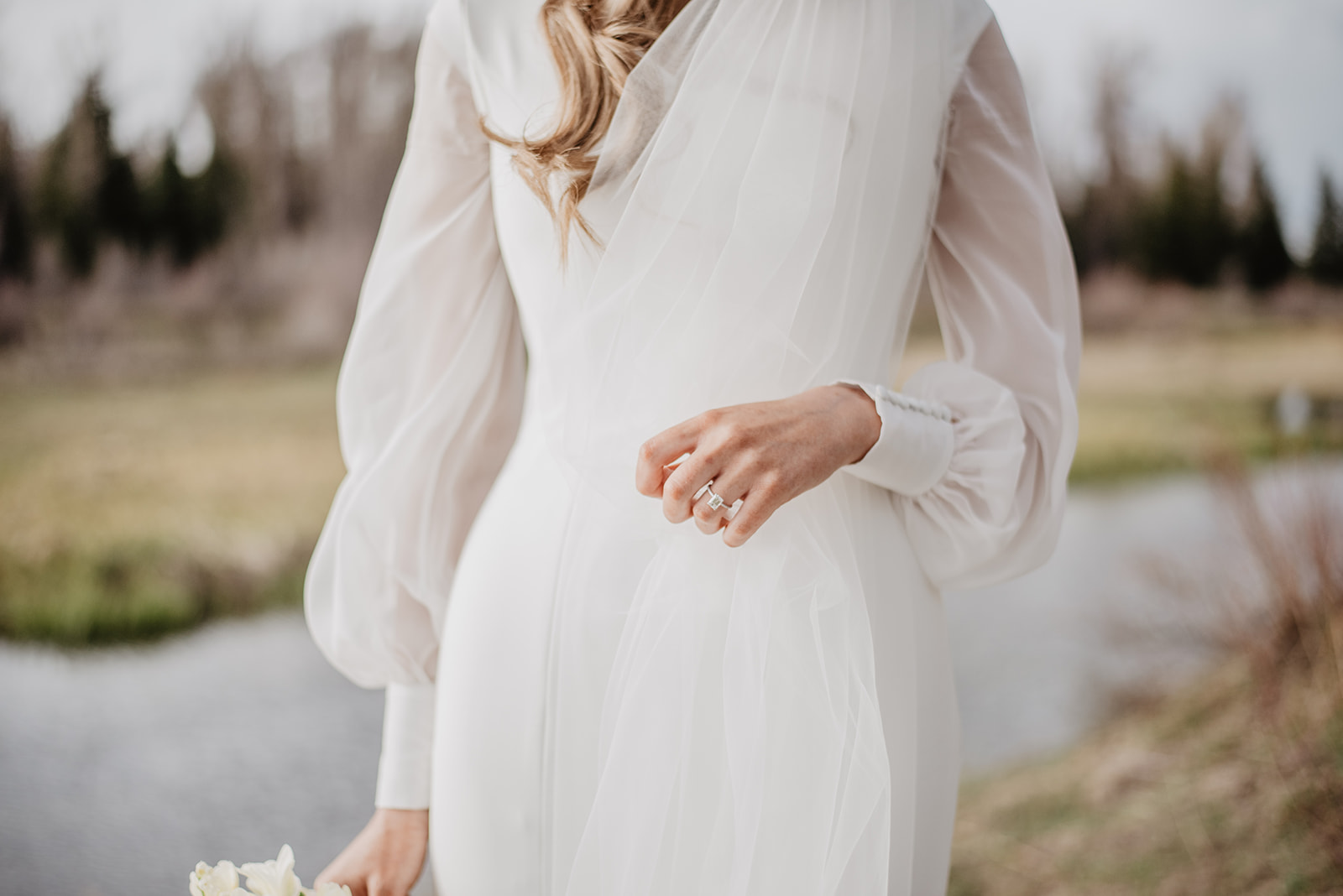 detail shot of brides sating white wedding dress as she holds her veil with one hand and her wedding florals with the other in Grand Tetons National park for her wedding