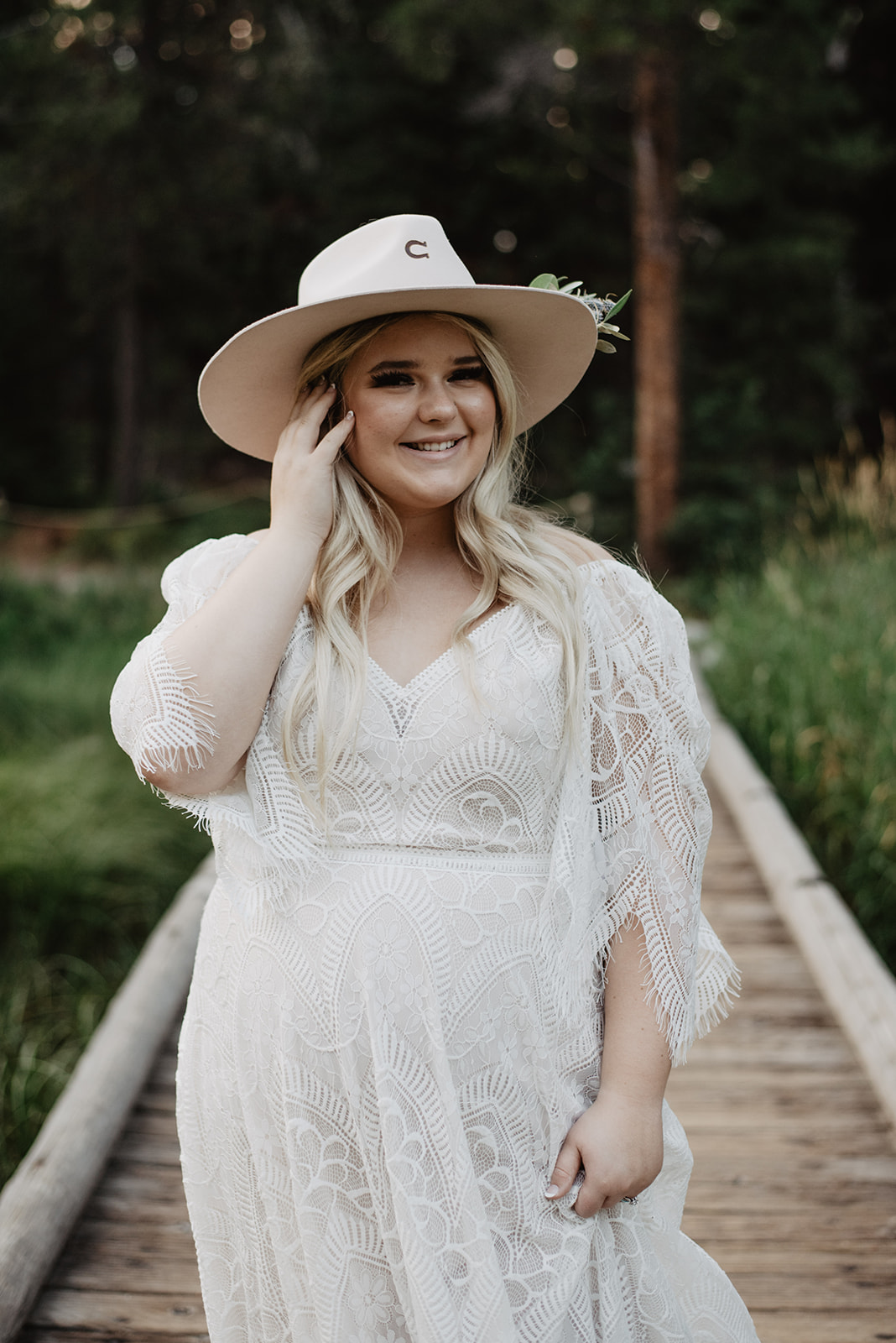 2022 wedding dresses with bride in a boho wedding dress and a cute wide brimmed hat smiling as she touches her hair in the Grand Tetons