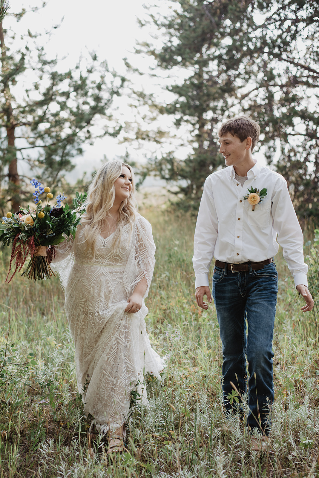 boho bride with a beautiful large lace wedding dress walking with her groom through a meadow in the Grand Tetons as she holds her custom floral wedding bouquet