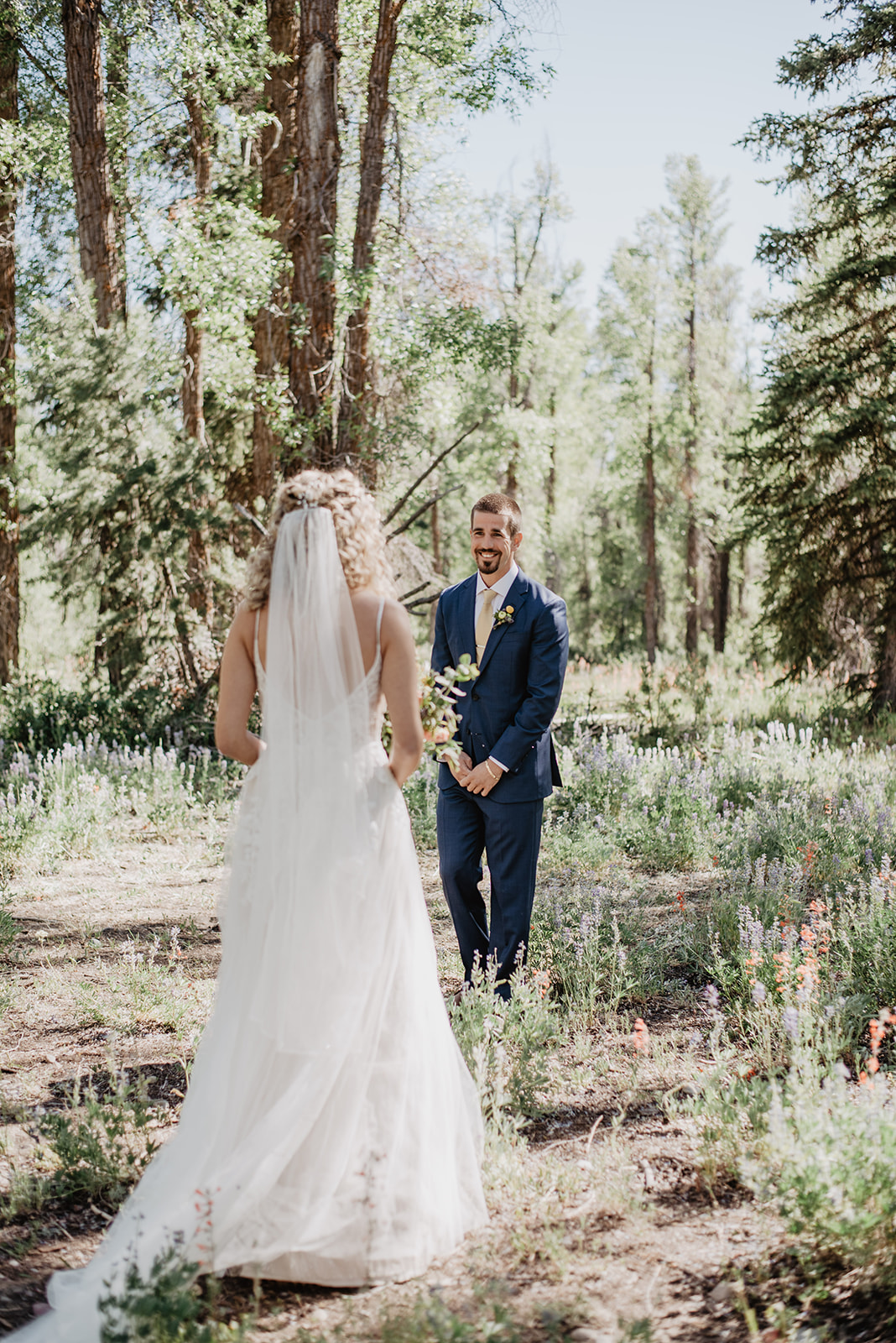 groom seeing his bride in her lace wedding dress in the woods of Jackson Hole for their elopement, captured by the best Jackson Hole wedding photographer