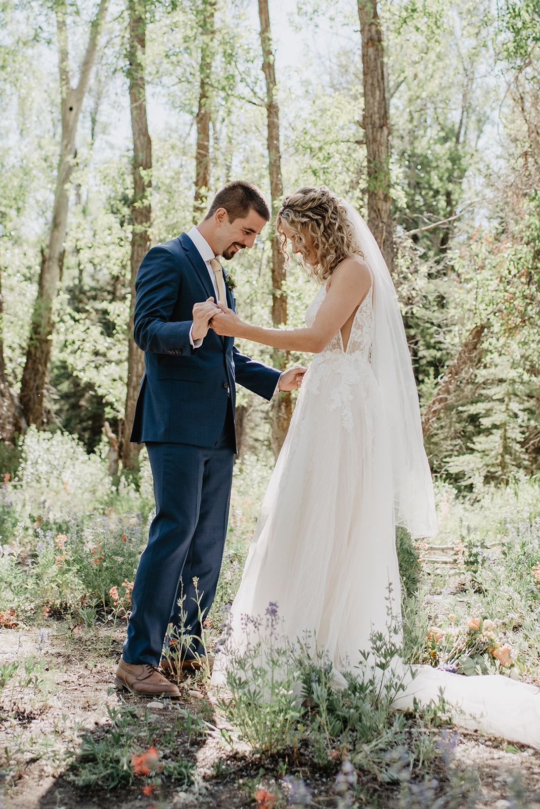 bride and groom holding hands together in JAckson HOle's forest as the groom looks at his brides lace white wedding dress