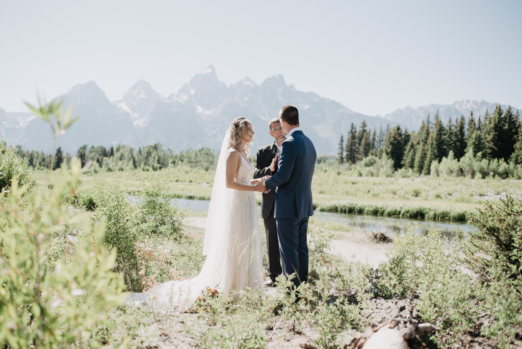 Jackson hole photographers capture blonde bride holding her groom hands as they smile during their ceremony in Jackson Hole with Grand Teton wedding and elopement photographer in the Spring