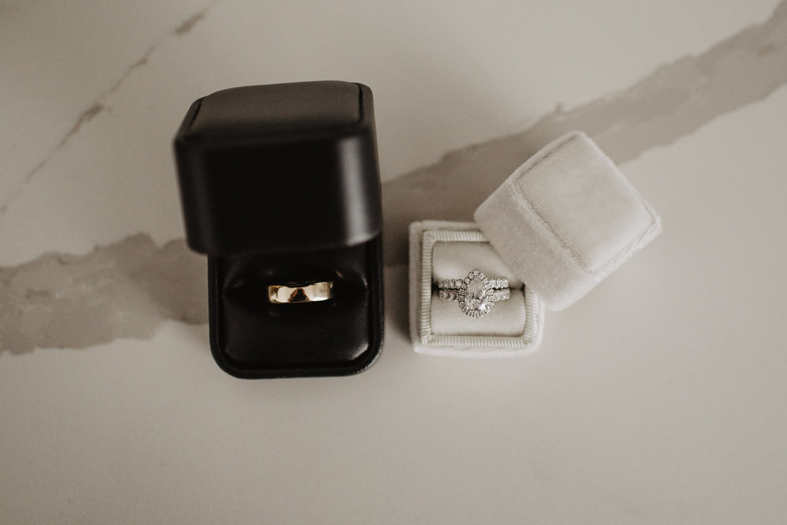 both bride and grooms wedding rings in their wedding boxes on a marble table top