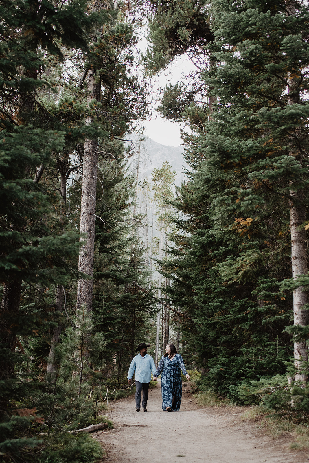 best wedding photographers in Jackson Hole capture man and woman walking through the woods for an engagement session after a surprise proposal.