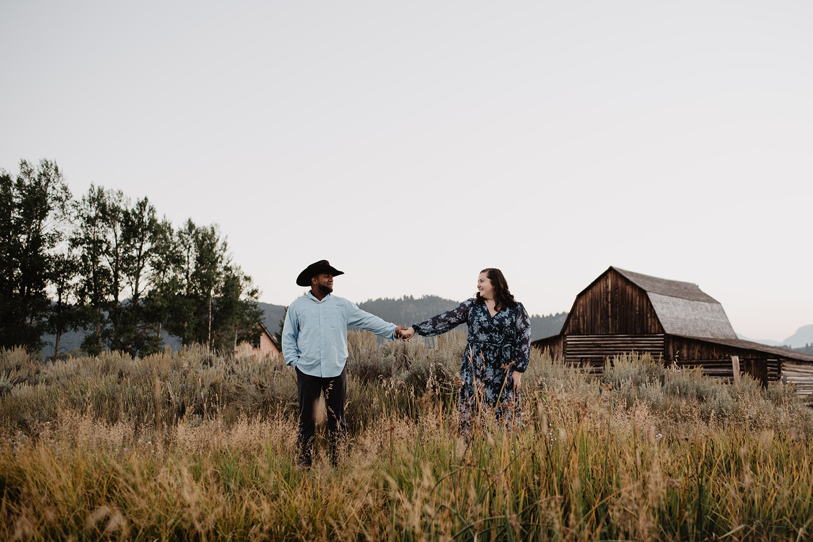 National Park proposal with mand nad woman holding hands and laughing at Mormon Row in the Tetons captured by best Jackson Hole wedding photographers