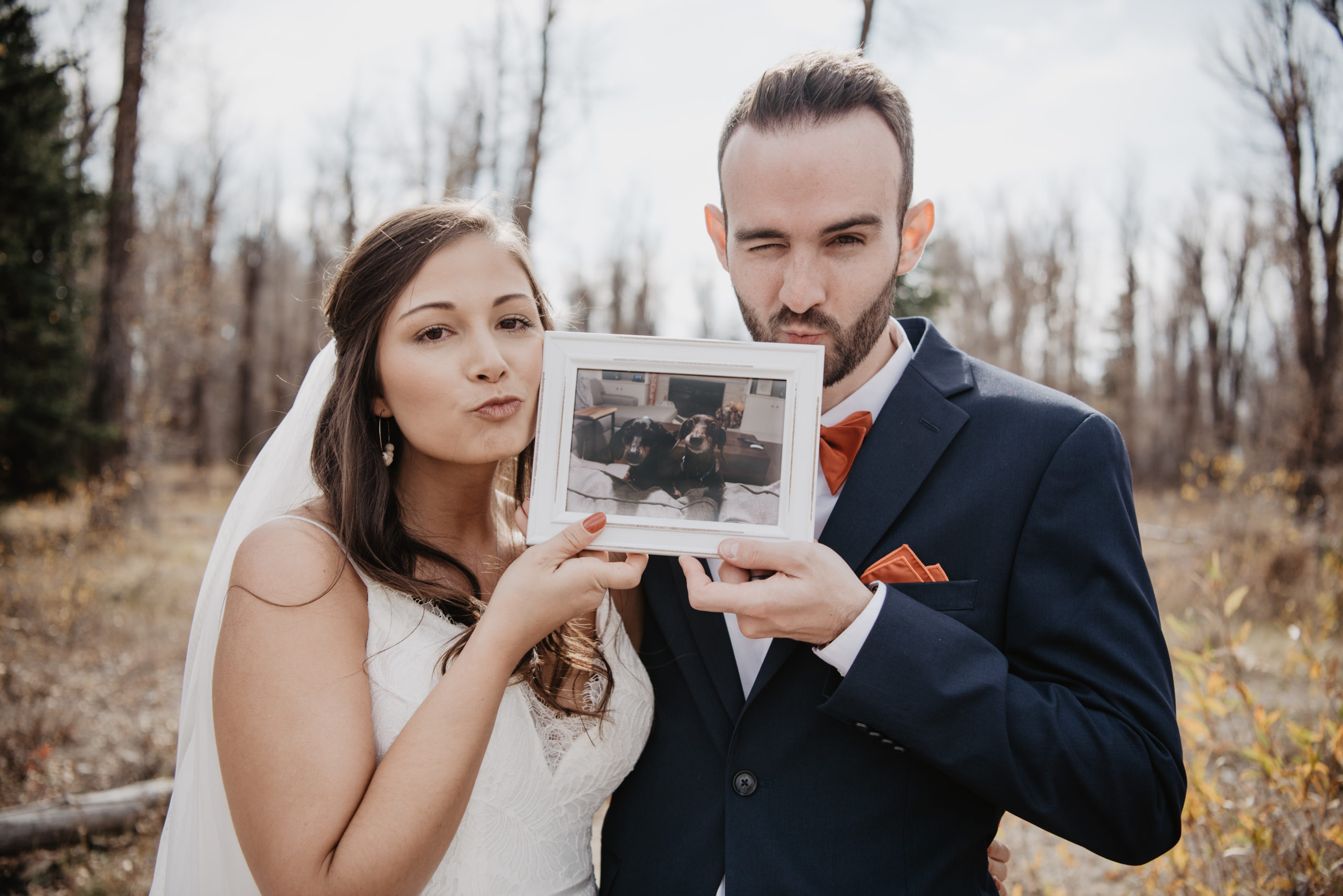 bride and groom holding a picture of their dog and kissing the frame to include their pet on their wedding day in Jackson Hole 