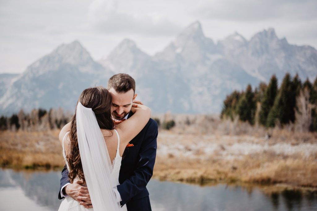 Jackson Hole photographers capture bride and groom hugging during their fall elopement in JAckson Hole with the Grand Tetons behind them for their wedding portraits