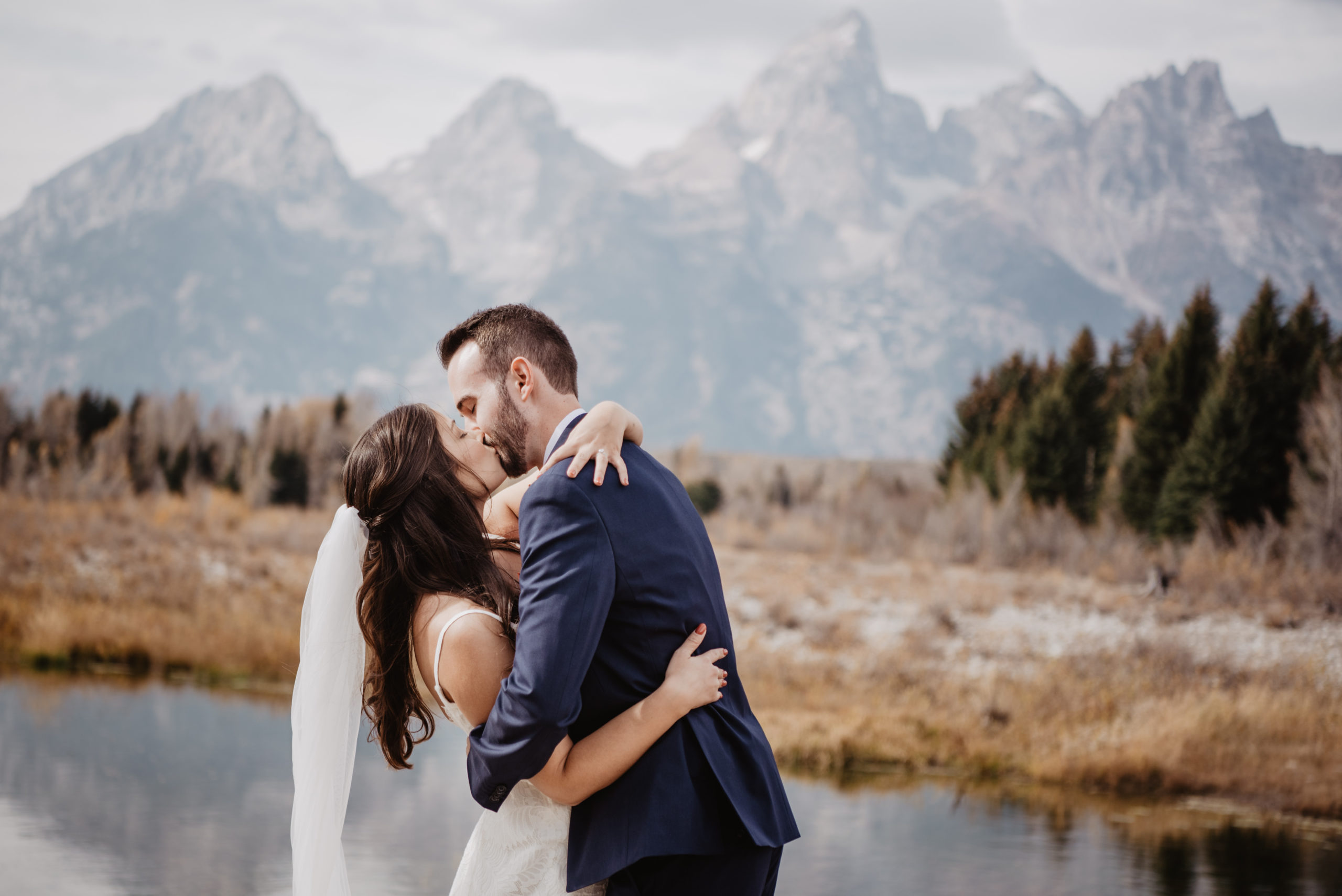bride and groom kissing as they embrace one another in the Tetons for their elopement with the mountain range behind them