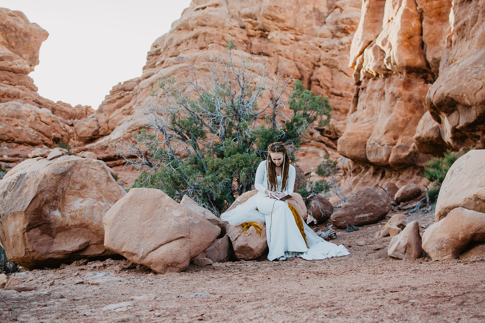 Eloping in Moab with bride sitting near some native brush and writing her vows in a notebook