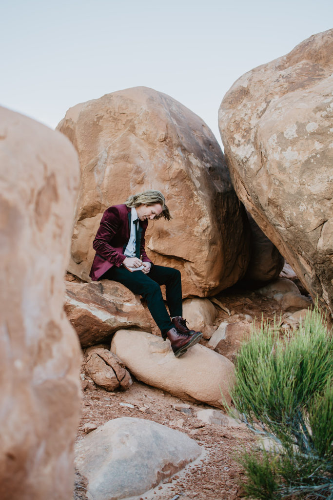 groom sitting on a red rock and writing his vows to his bride during their outdoor elopement in Moab Utah 