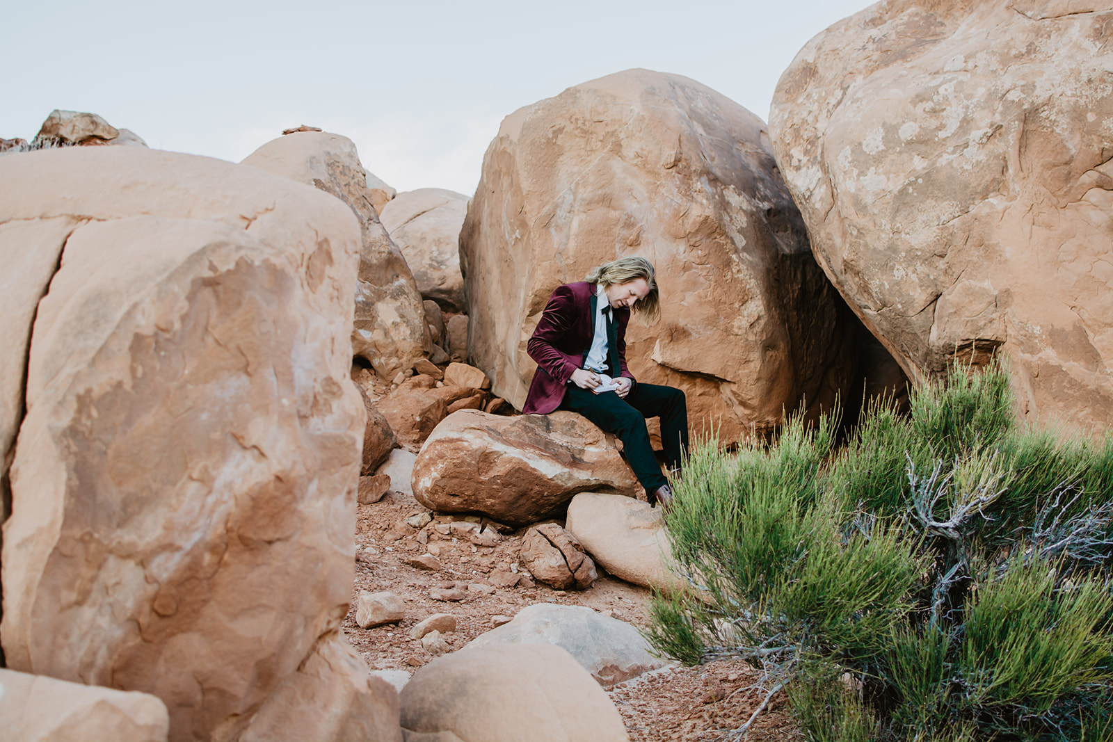 groom sitting on a rock and writing his vows in a leather bound book in Moab for his elopement