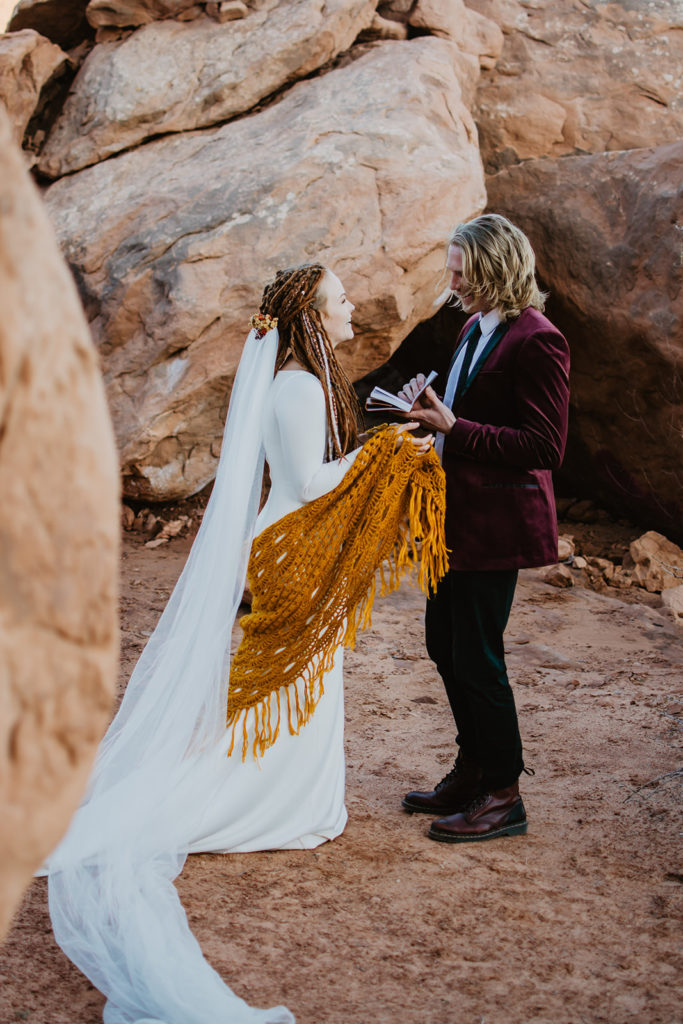 bride reading her private vows to her groom as they stand in the red rocks of Utah together with Moab wedding photographer 
