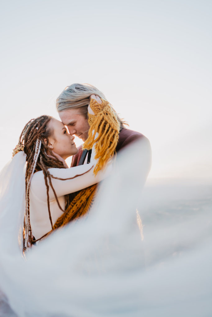 Moab elopement with bride and groom wrapped up in the brides veil while they embrace each other in the red rocks