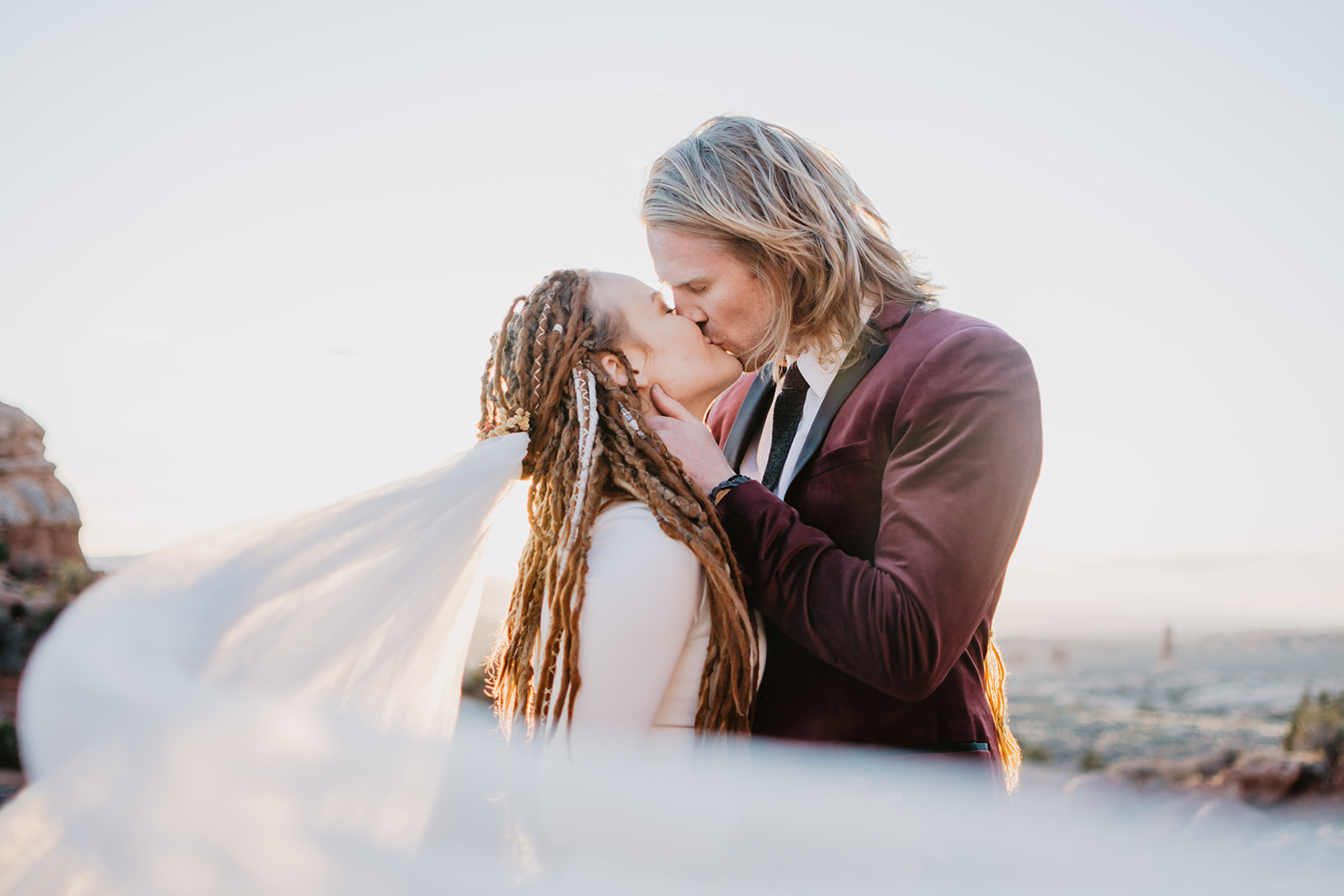 Arches National Park elopement with best Moab wedding photographer, bride and groom kissing as the sunset s behind them and the brides veil blows in front of the couple