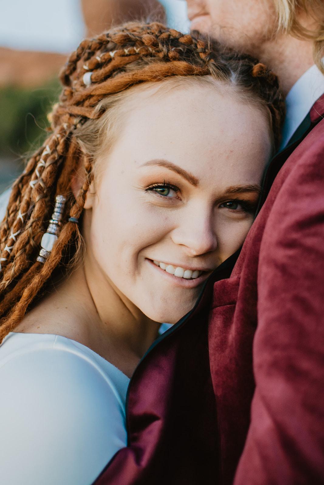 boho bride with red dreads leaning on her grooms chest as she smiles at the camera in Moab