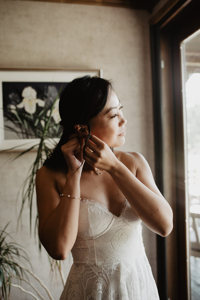 bride putting on her earrings as she looks out a window while in her bridal suite captured by Jackson Hole photographer