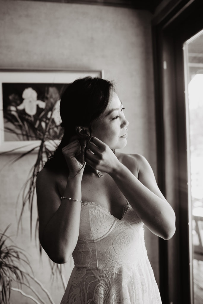bride looking out a window as she puts on her earrings as she gets ready for her Jackson Hole wedding day