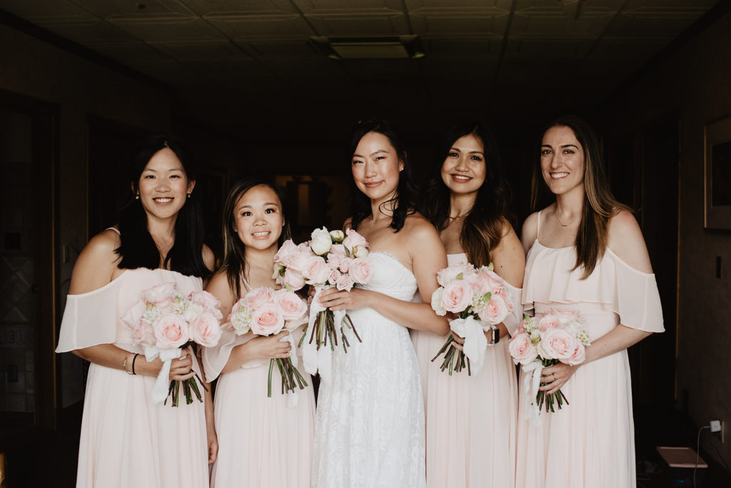 bridesmaids in light pink bridesmaids dresses while holding their rose bouquets together 