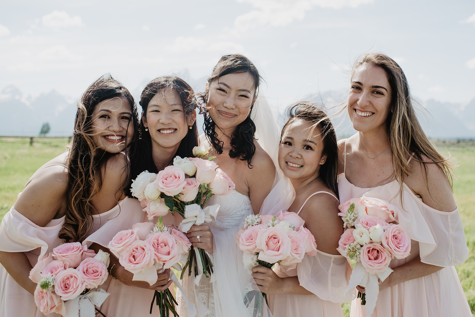 bride standing with her bridesmaids who are in light pink dresses posing with their pink rose wedding bouquets in the Tetons at Lost Creek Ranch