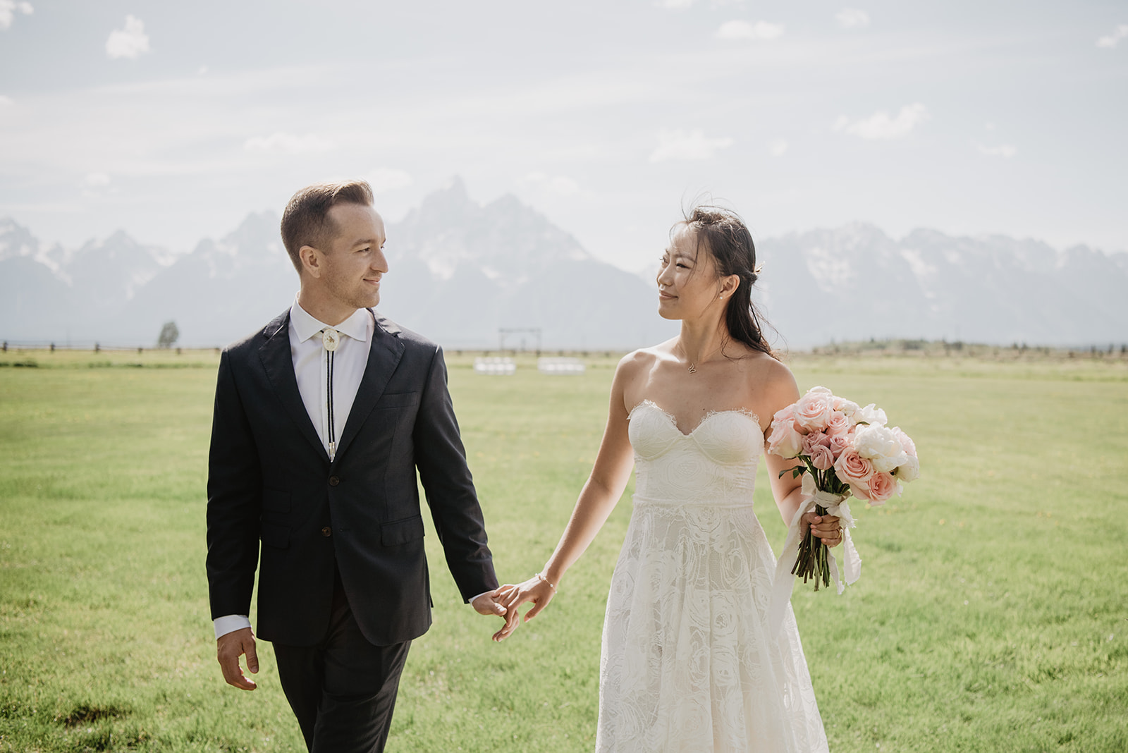 Summer wedding in Jackson Hole at Lost Creek Ranch with man and woman holding hands and walking together in a green pasture 