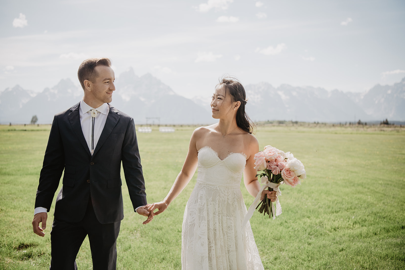 bride and groom holding hands as they walk together in a green field in Jackson Hole for their summer wedding