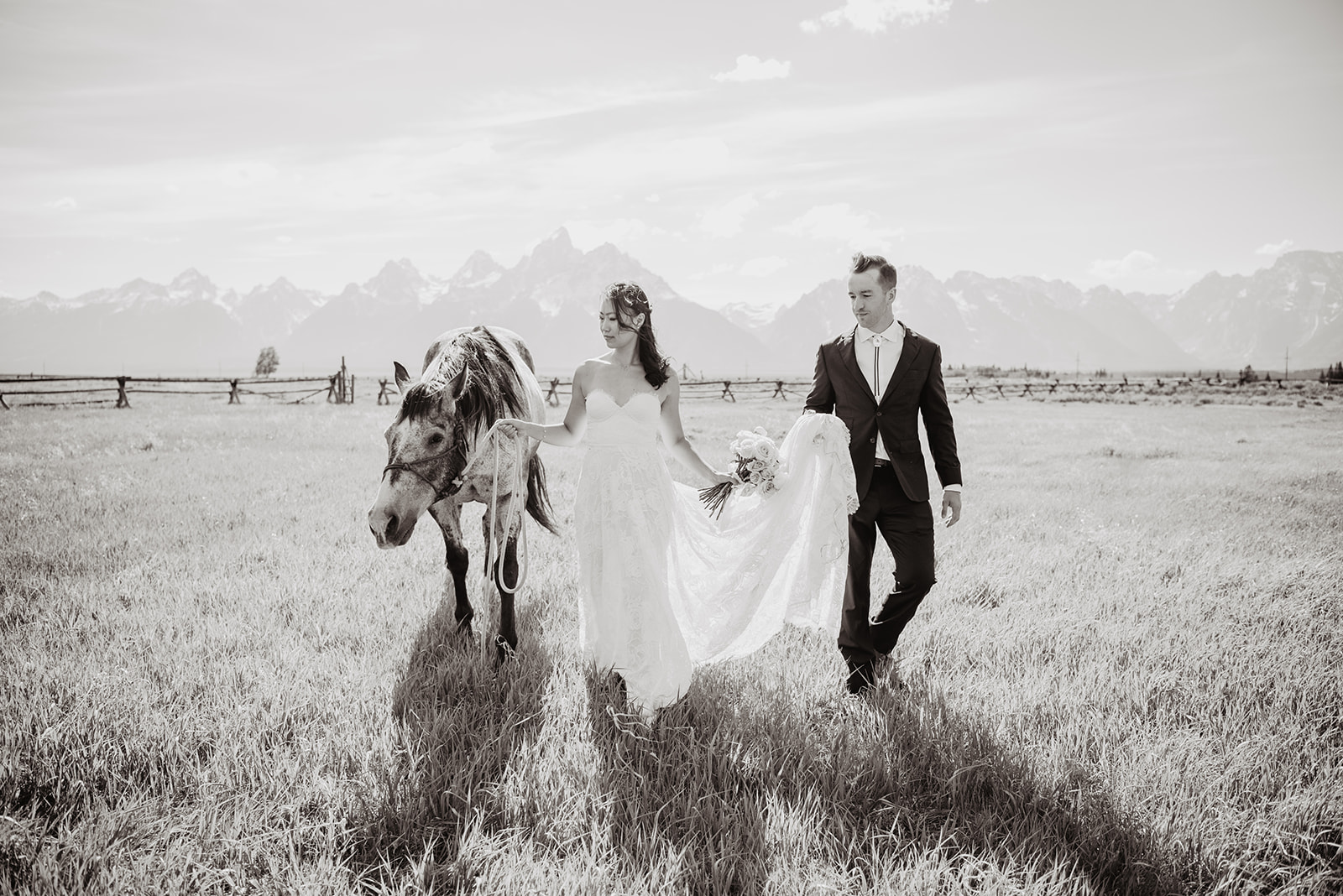 black and white image of bride and groom walking in a meadow with a horse at Lost Creek Ranch 