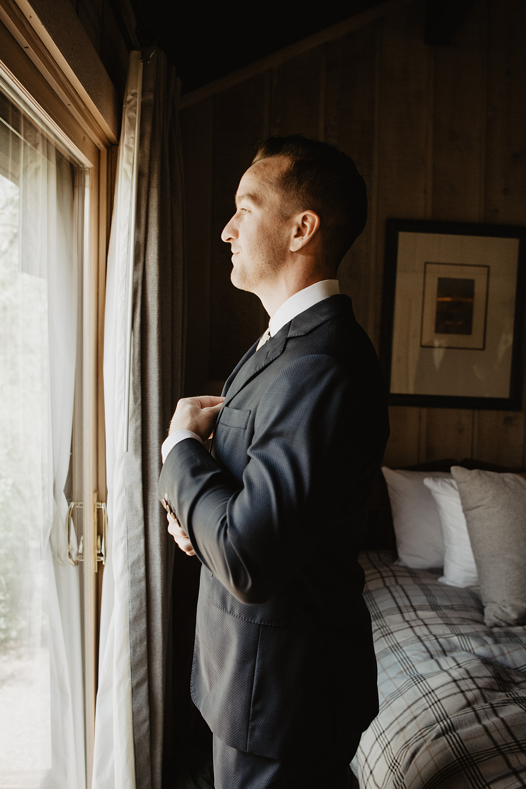 groom adjusting his tie as he looks out the window in his room as he gets ready for his Jackson Hole wedding