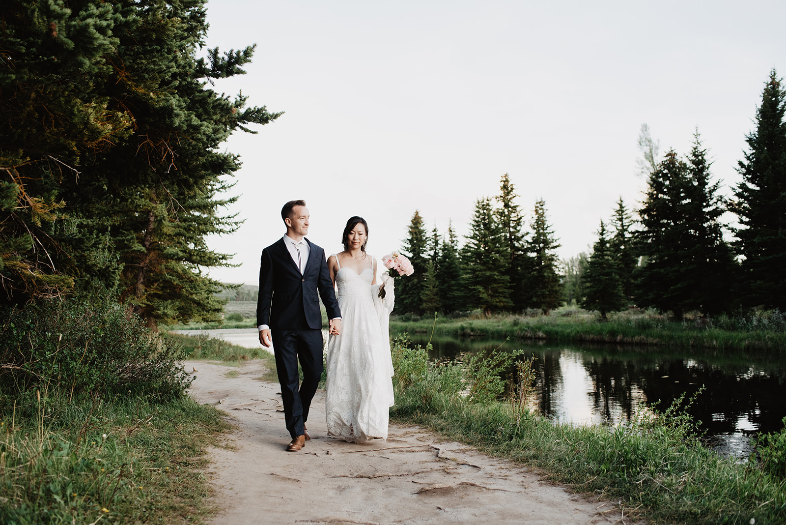 bride and groom strolling next to a creek in Jackson Hole on their wedding day in the summer