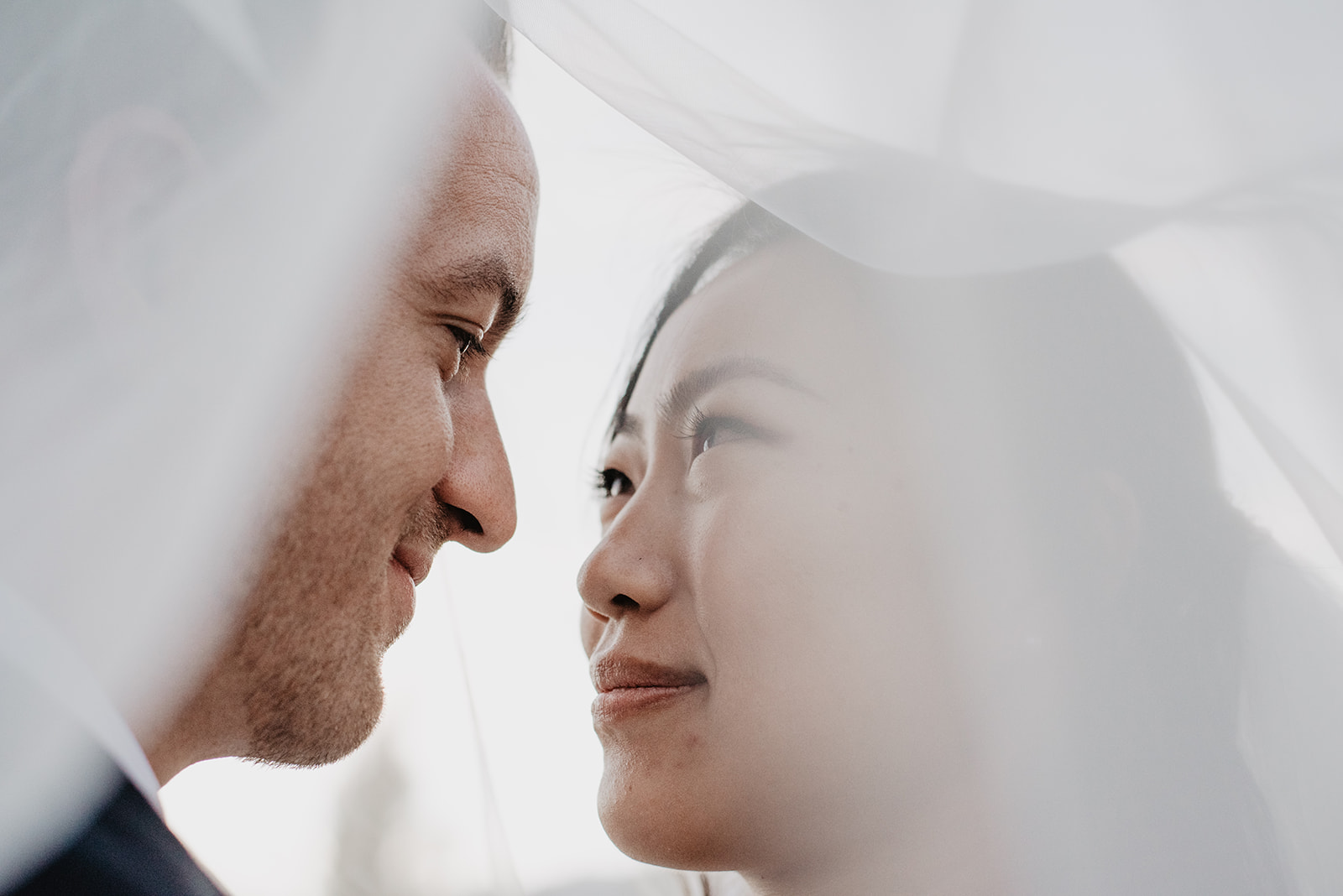 intimate wedding photo with bride and groom under their wedding veil looking into each others eyes