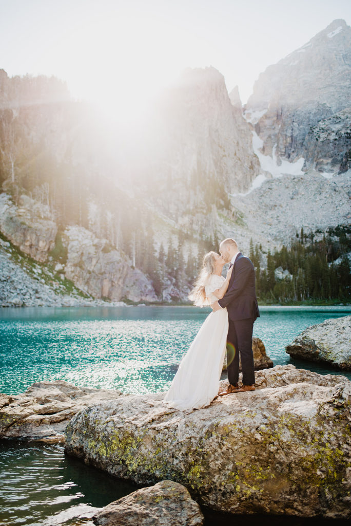 bride and groom embracing on the top of a mountain in the Grand Tetons for their wedding photos with the bright bue water of a lake behind them