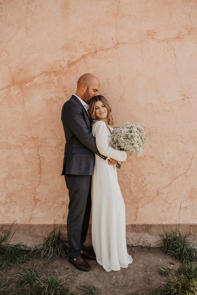 groom standing behind woman and holding her waist as she smiles over her shoulder to her groom and holding a bouquet in a Jackson Hole elopement locations