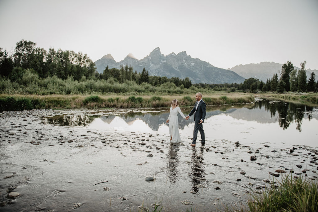 Grand Teton National Park elopement with bride and groom walking through a river bed with the mountains in the background