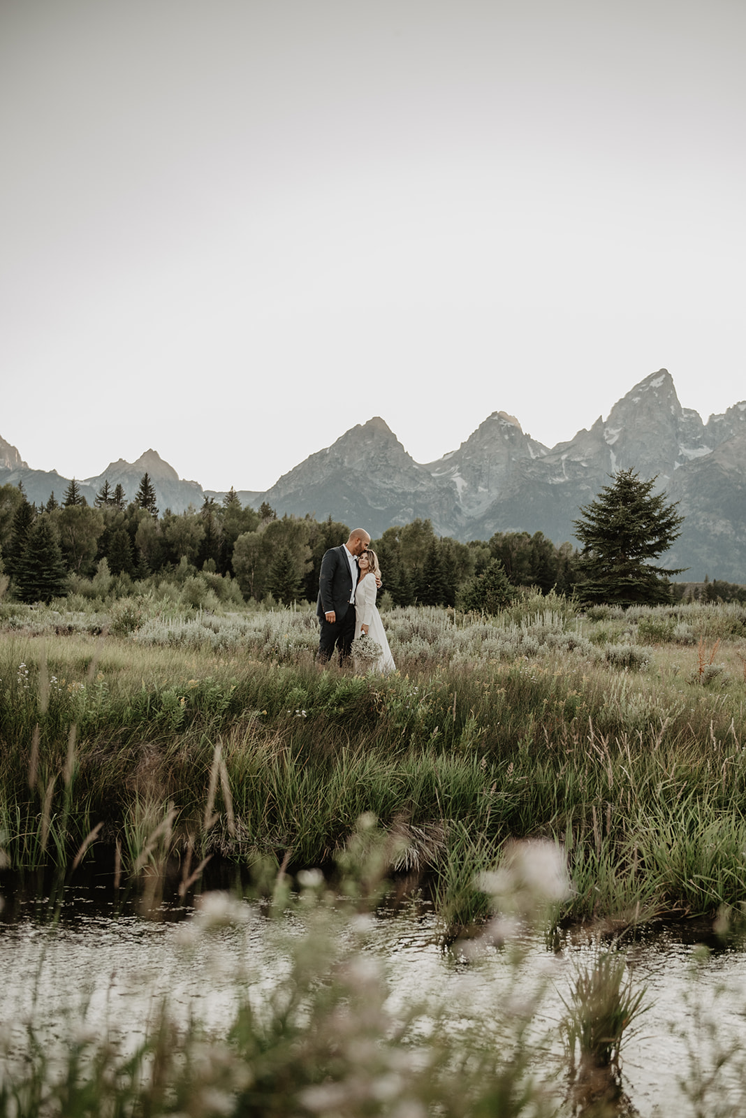 bride and groom embracing in a field together in front of the Tetons for their outdoor elopement with Jackson Hole photographer 
