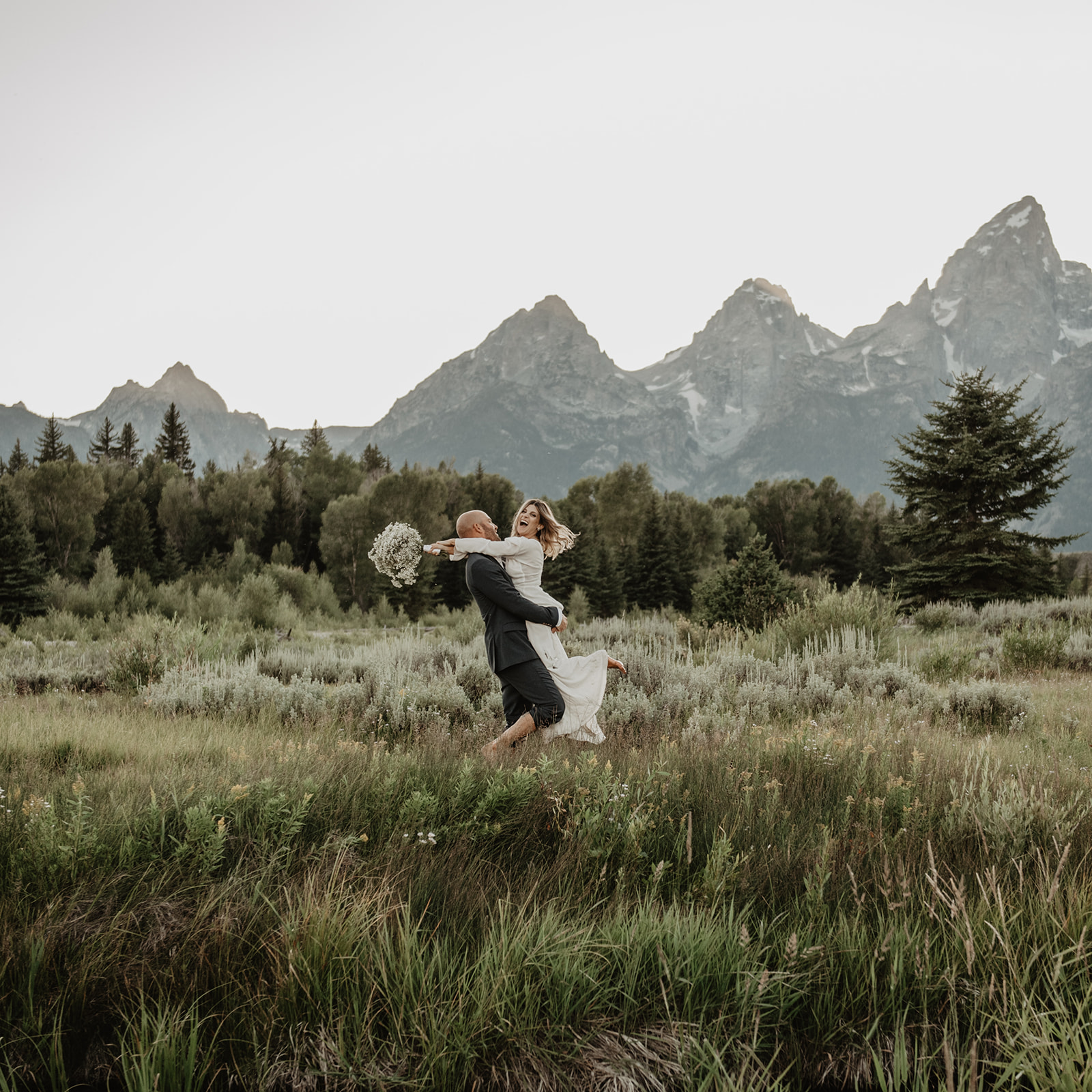bride and groom dancing in a meadow in the Grand Tetons on their wedding day as they hike through the trails