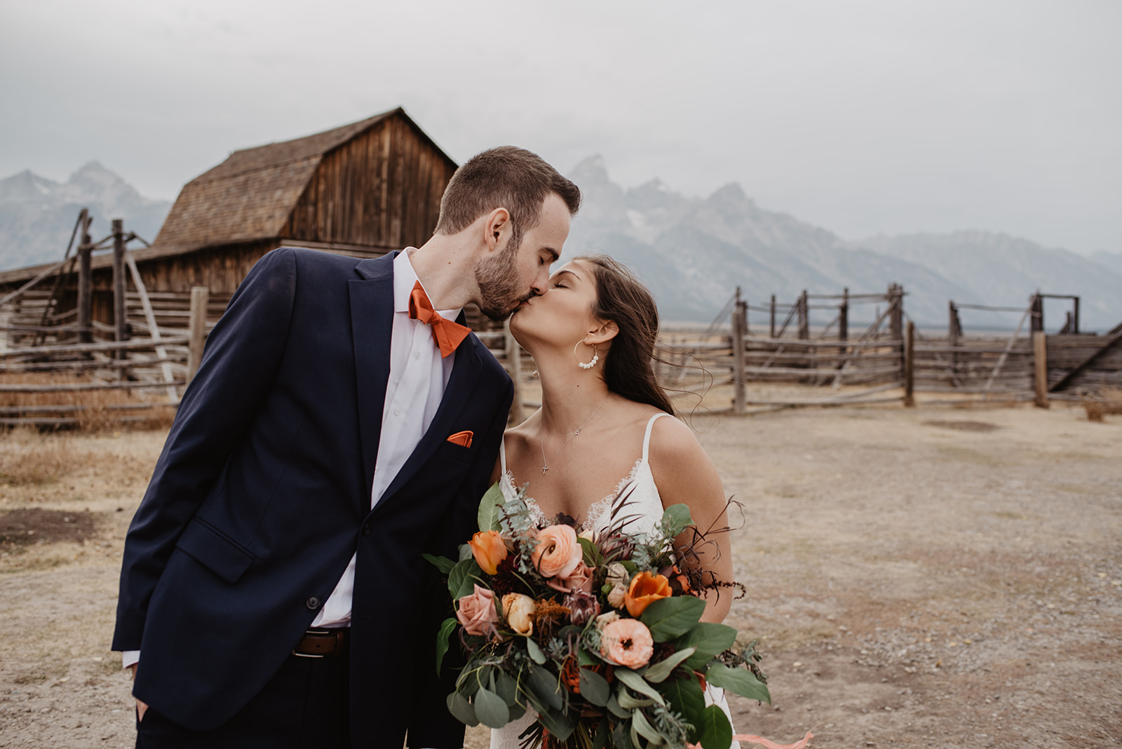 bride and groom in Jackson Hole kissing in front of an old barn with the Tetons in the background