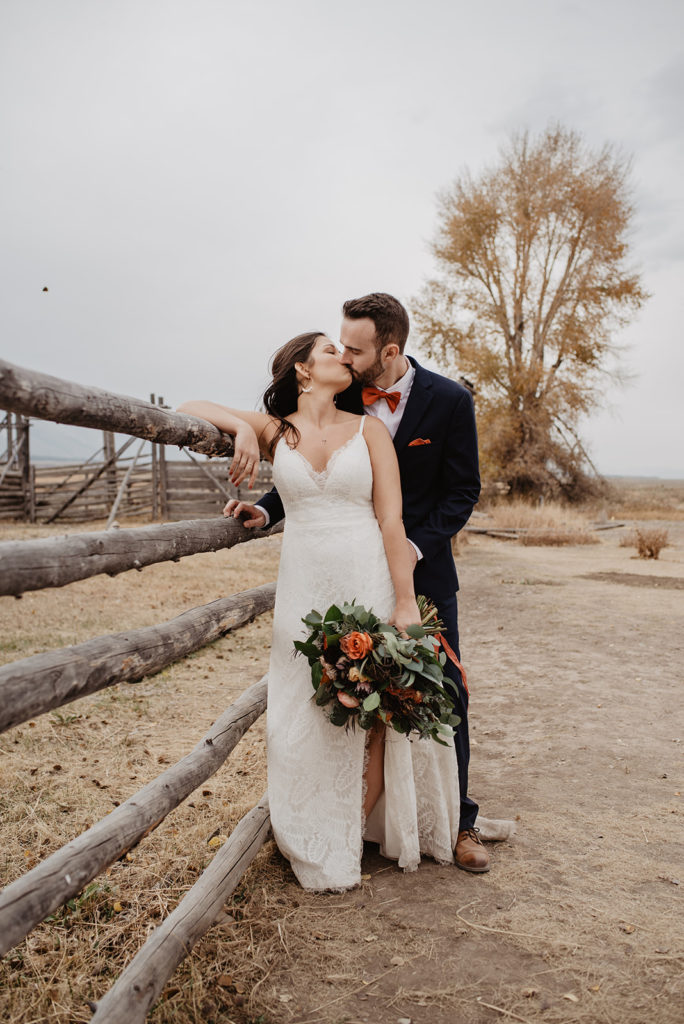 outdoor fall wedding in Jackson Hole with bride and groom embracing as they lean against a fence together and kiss photographed by Jackson Hole wedding photographer 