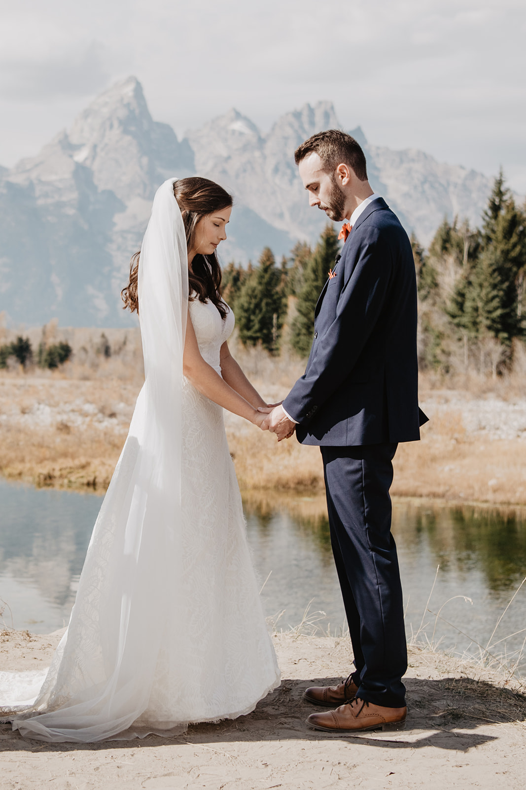bride and groom holding hands as they prayer together at their Jackson Hole wedding ceremony with the Tetons behind them